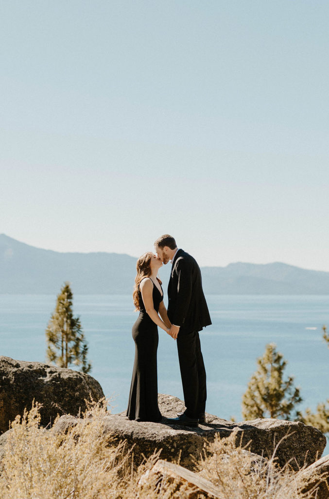 Engagement couple in formal attire kissing while standing on rock together at Lake Tahoe