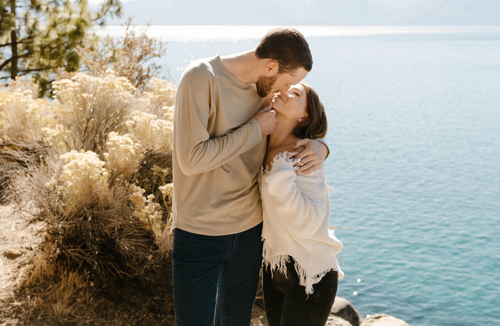 Engagement couple with arms around each other almost kissing with Lake Tahoe in background