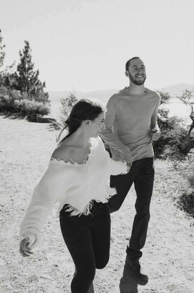 Engagement couple laughing while running down dirt trail together in Lake Tahoe