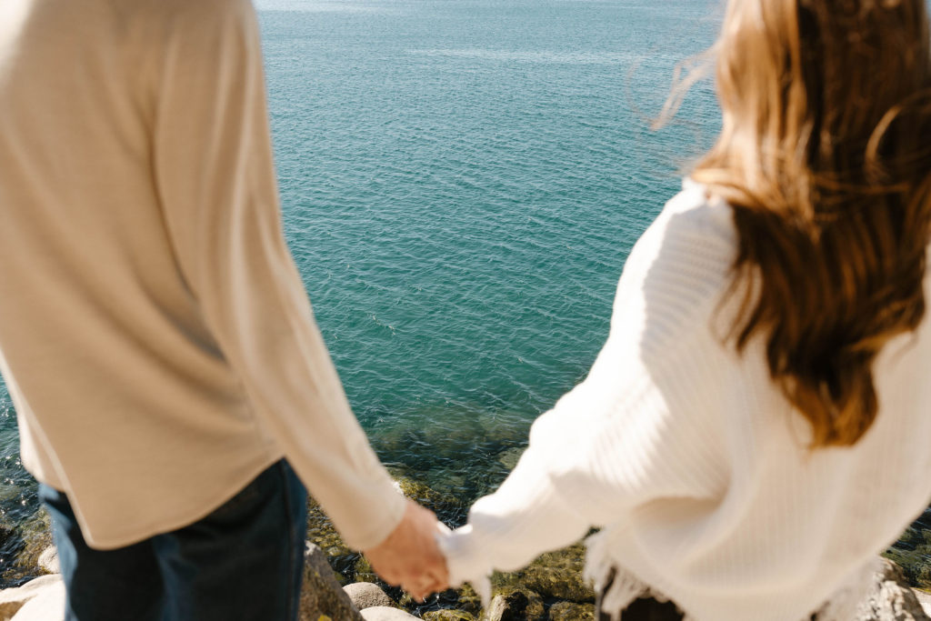 Engagement couple standing together holding hands looking at Lake Tahoe