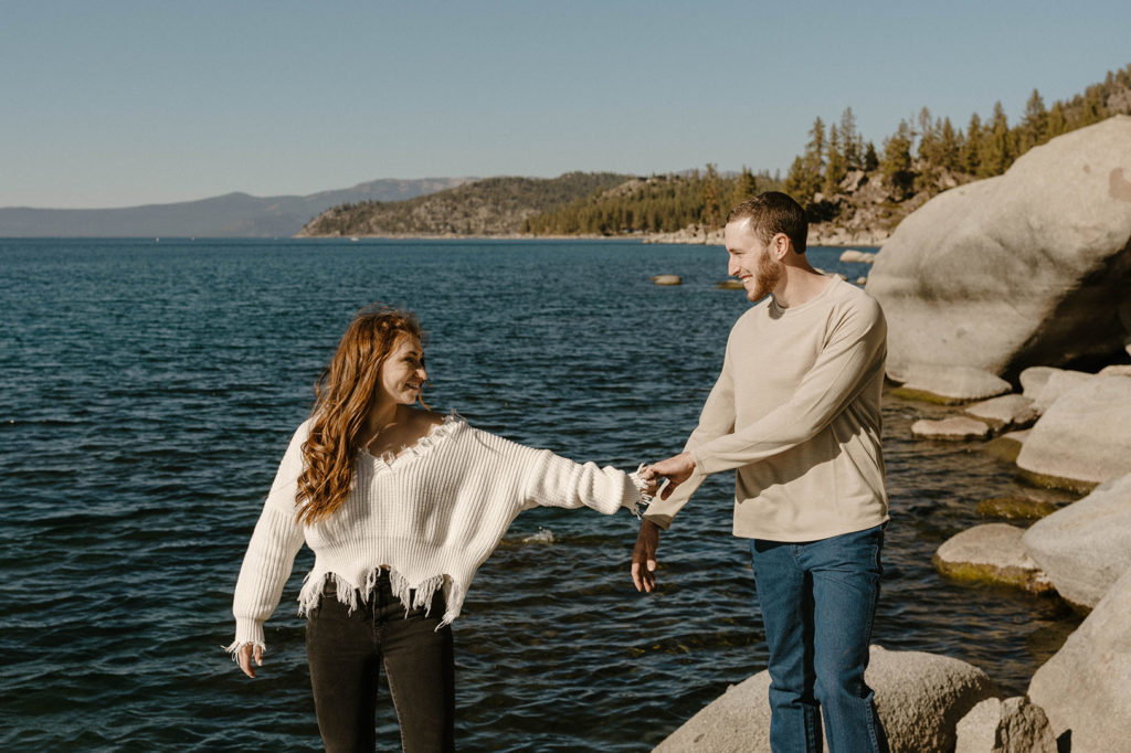 Engagement couple holding hands while walking along large rocks together along Lake Tahoe 