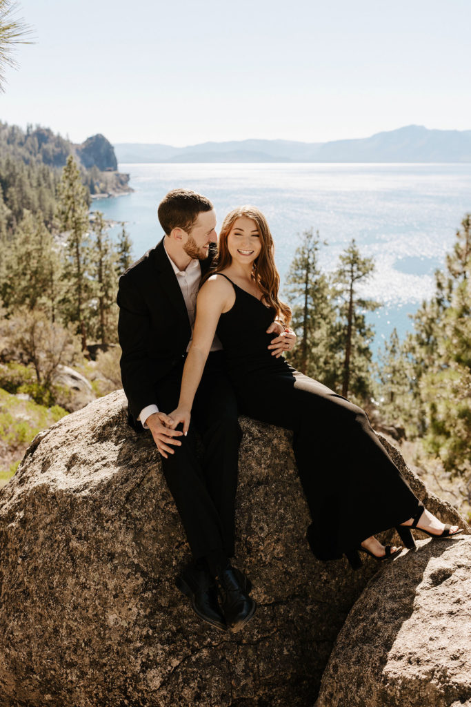 Engagement couple holding each other while smiling and sitting on rocks at Lake Tahoe
