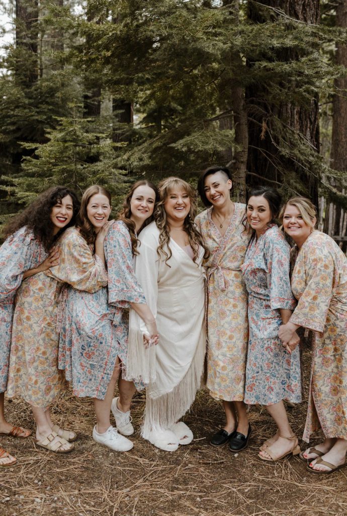 Wedding bride and bridal party in robes standing together and smiling outside in forest in Lake Tahoe
