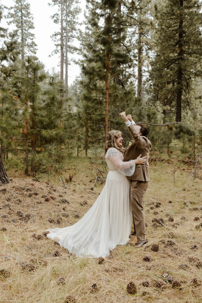 Wedding groom celebrating while bride laughs and holds him during first look in forest in Lake Tahoe