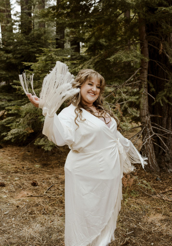 Wedding bride playing with dress sleeves while smiling at camera in forest in Lake Tahoe