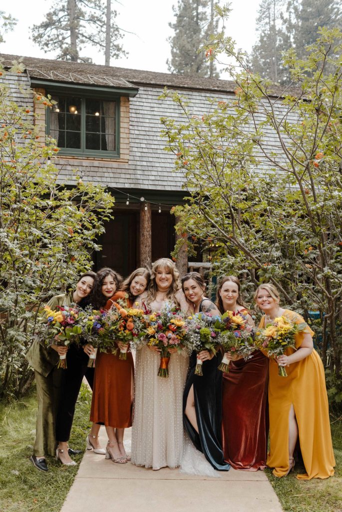 Wedding bride and bridesmaids smiling together at camera while holding flower bouquets in Lake Tahoe
