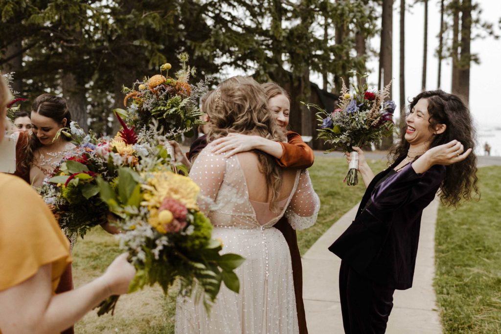 Wedding bride hugging bridesmaid while another laughs after ceremony outside in Lake Tahoe