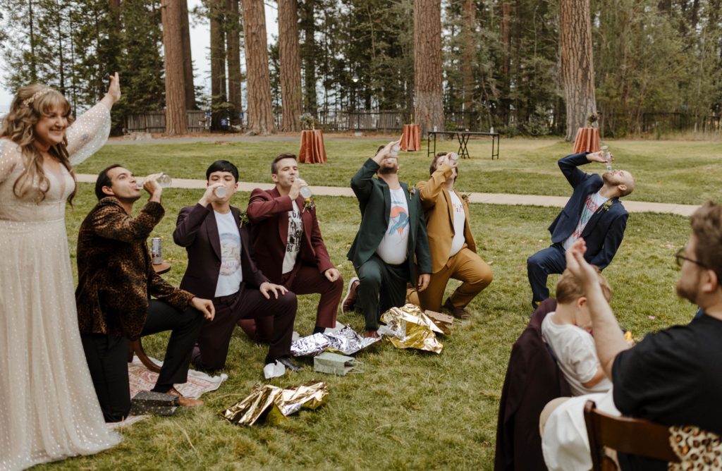 Wedding groomsmen getting iced chugging beer on one knee while bride smiles outside in Lake Tahoe