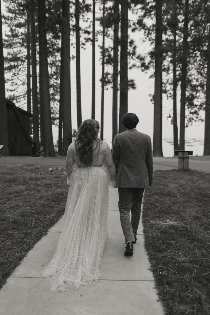 Wedding couple holding hands and walking away from camera on sidewalk outside in Lake Tahoe