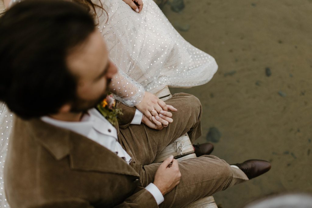 Wedding couple hands holding each other while sitting together on pier in Lake Tahoe