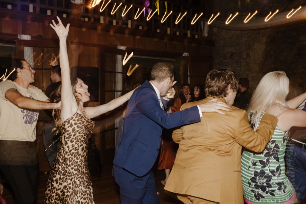 Wedding guests with arms on each others shoulders dancing and marching along dance floor during reception at valhalla in Lake Tahoe
