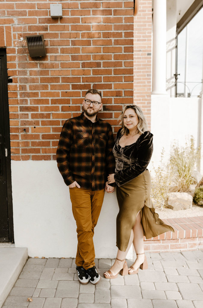 couple holding hands and smiling in front of a brick wall in reno