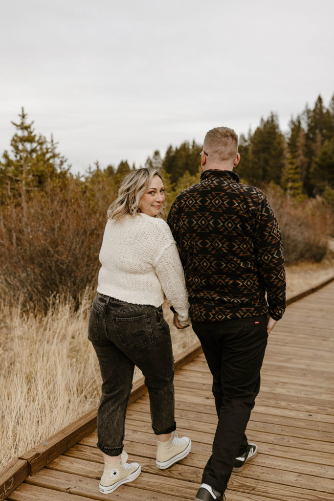 couple smiling and walking on a path in a meadow in lake tahoe for their engagement photos