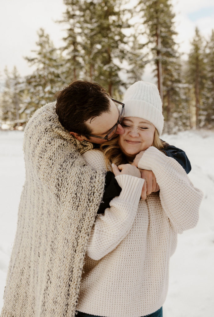 couple hugging and kissing in the snow for their winter lake tahoe engagements