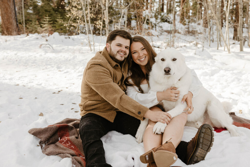 couple sitting on a blanket in the snow with their dog