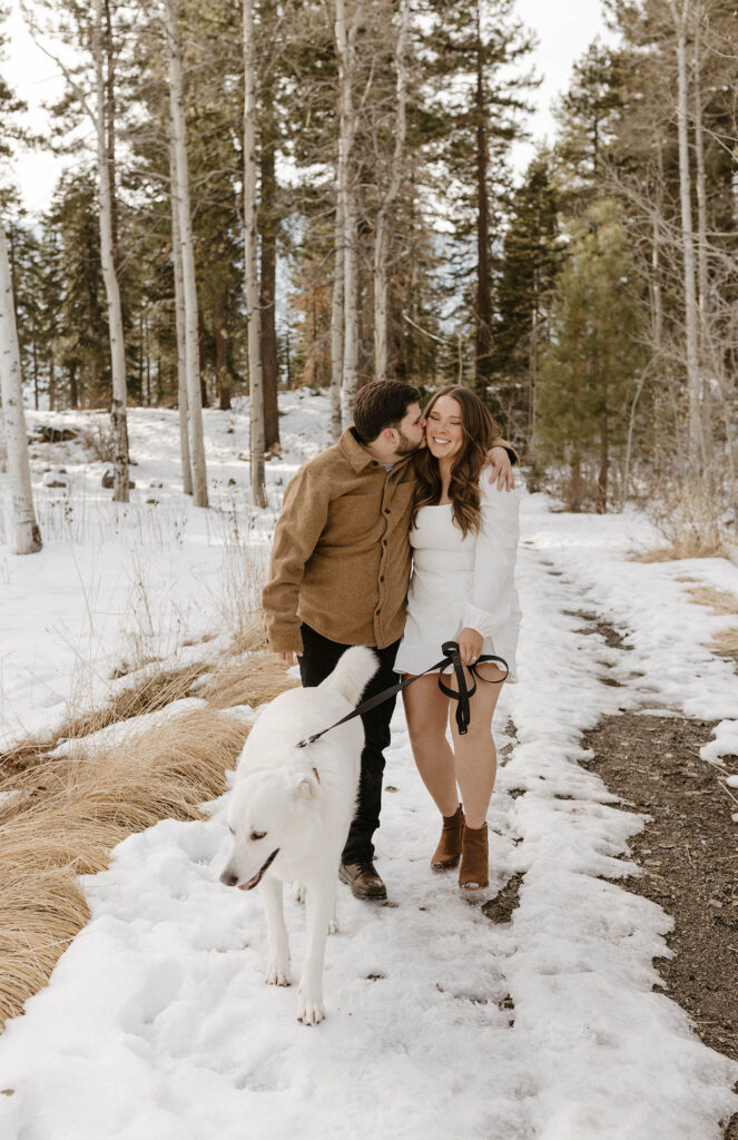 engagement couple walking in the snow with their dog