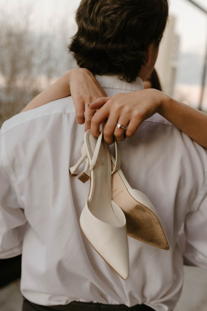 woman holding heels and showing engagement ring while hugging her fiance
