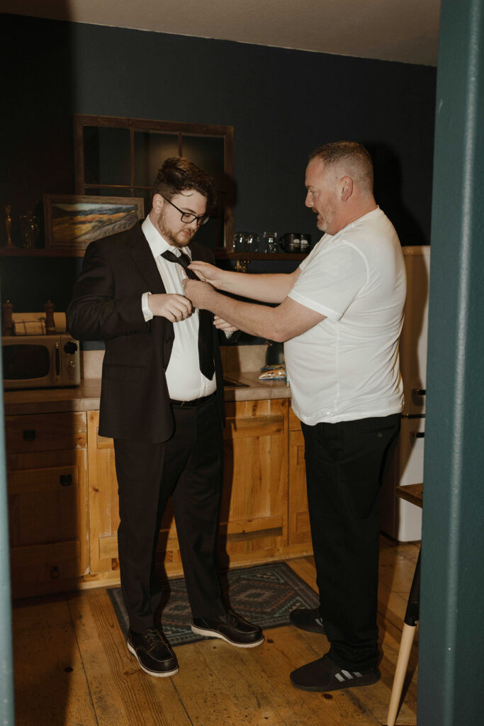 the groom's dad helping him put his tie on inside a cabin in lake tahoe