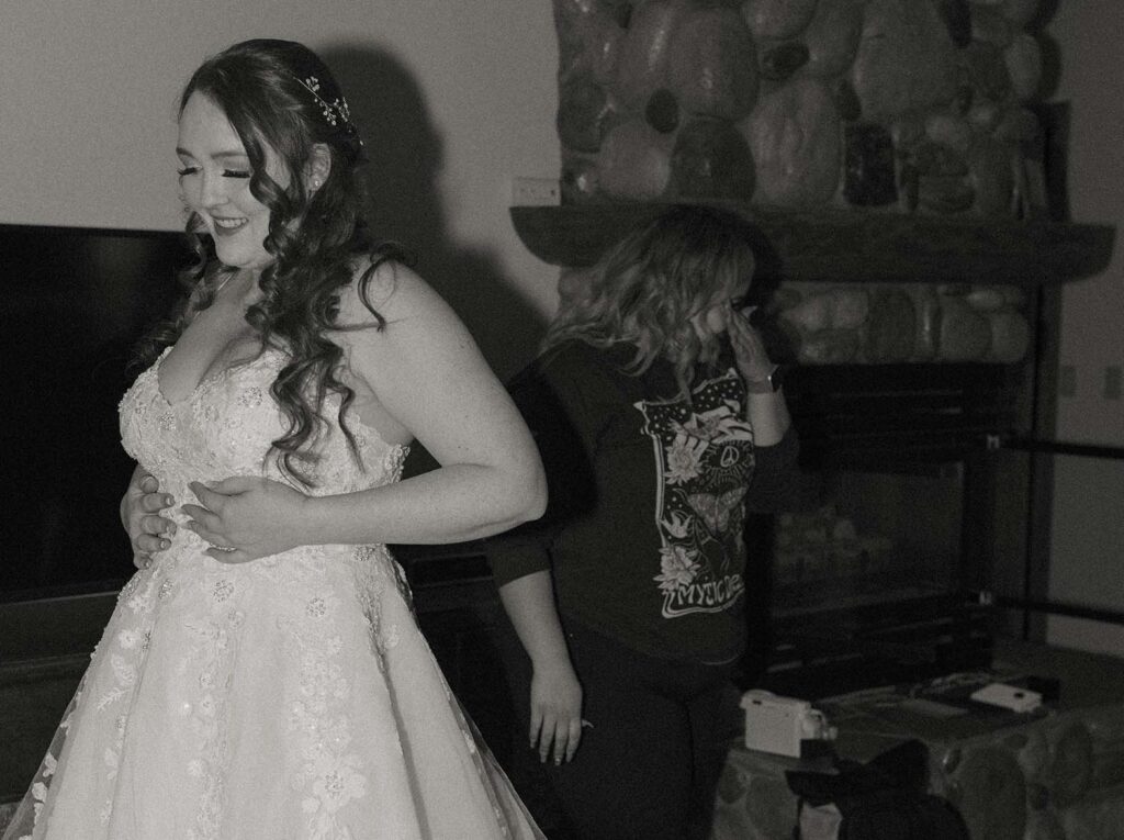 bride putting her dress on while her friend wipes tears
