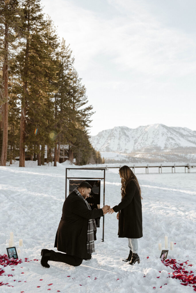 man on one knee putting a ring on a woman in the snow in lake tahoe