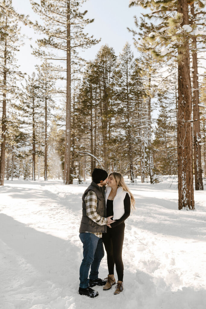 maternity couple holding belly and smiling in lake tahoe in the snow