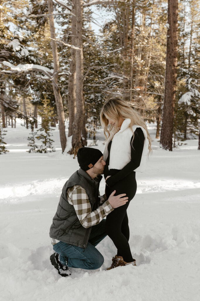 man kissing pregnant woman's belly in the snow in lake tahoe