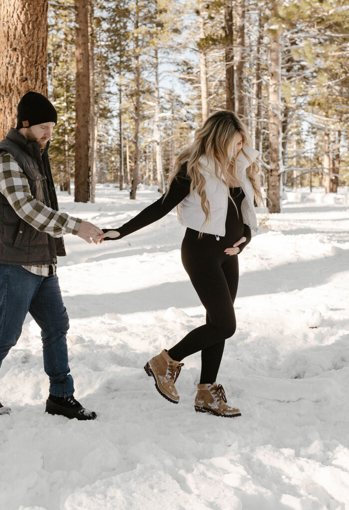 woman holding pregnant belly and holding her husband's hand while walking in lake tahoe