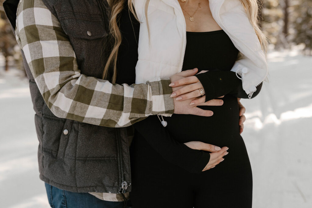 maternity couple holding belly in the snow in lake tahoe
