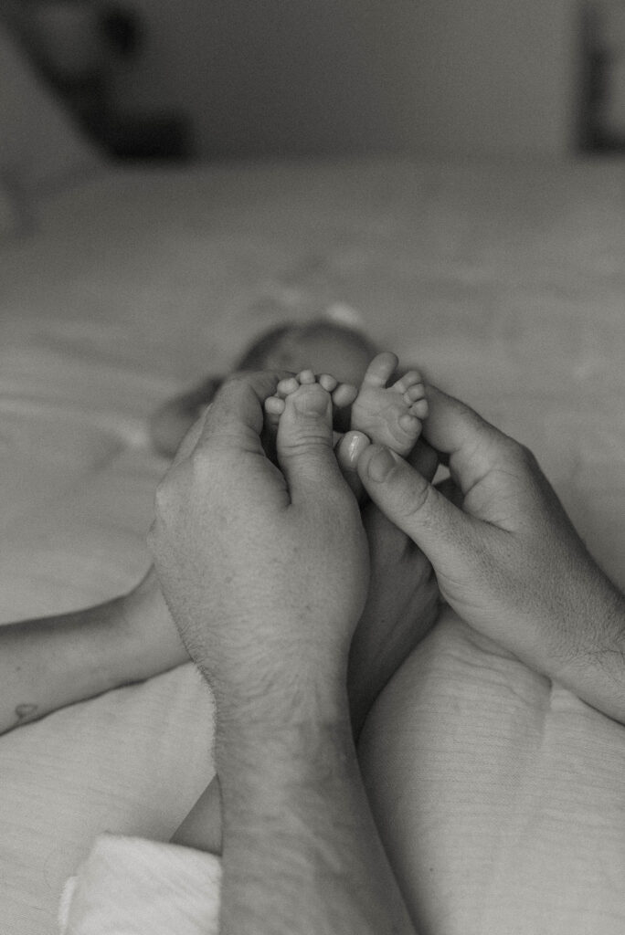 Mom and Dad's hands holding baby's feet inside home