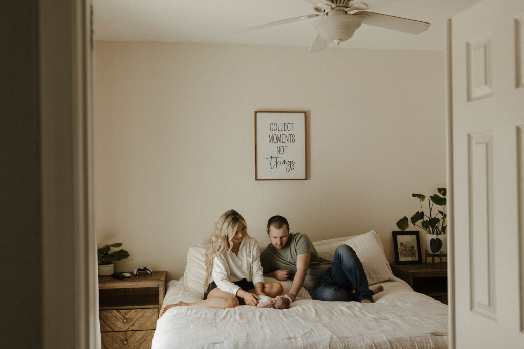 Couple sitting on bed inside home playing with baby on her back