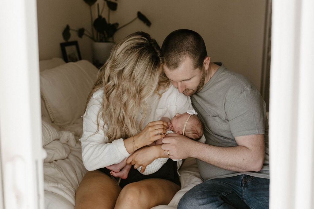 Couple holding baby together and looking down at her while on bed inside home