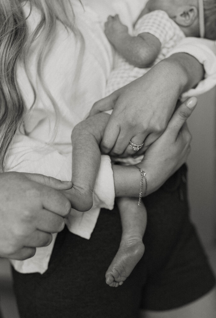 Couple holding baby's leg and foot while wearing wedding rings inside home