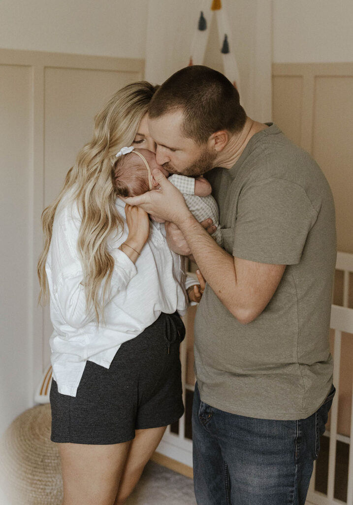 Couple holding and kissing baby in front of crib inside home