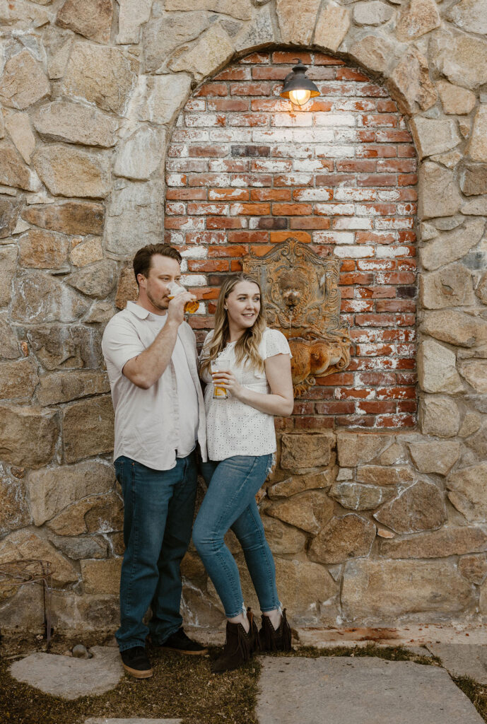 Engagement couple leaning against stone wall while sipping beer in virginia city
