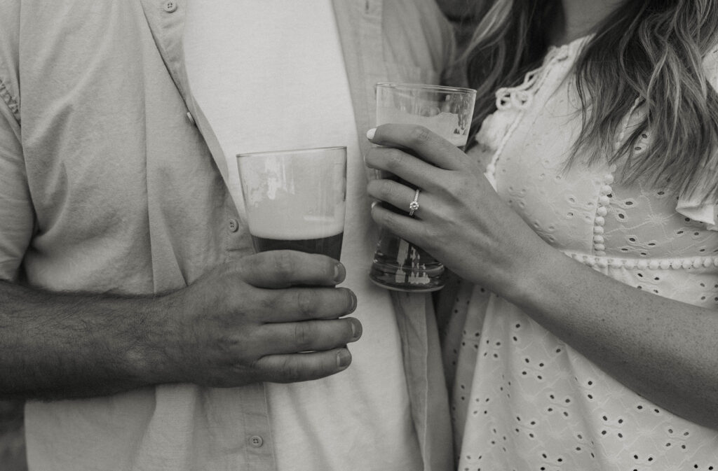 Close up of engagement couple holding beers with engagement ring