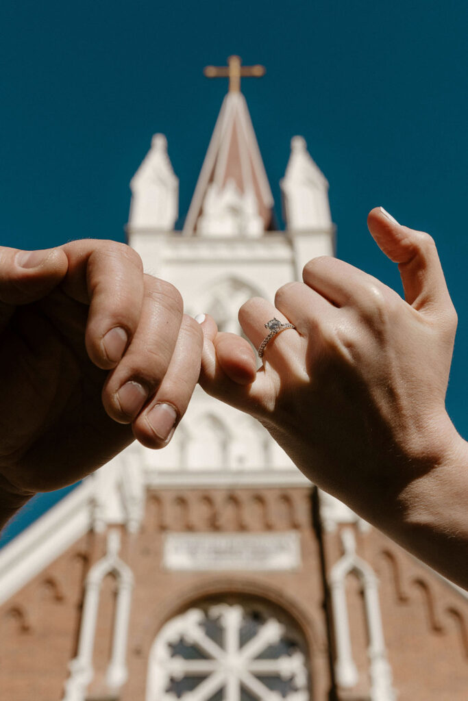 Engagement couple holding fingers with engagement ring in front of chapel in virginia city