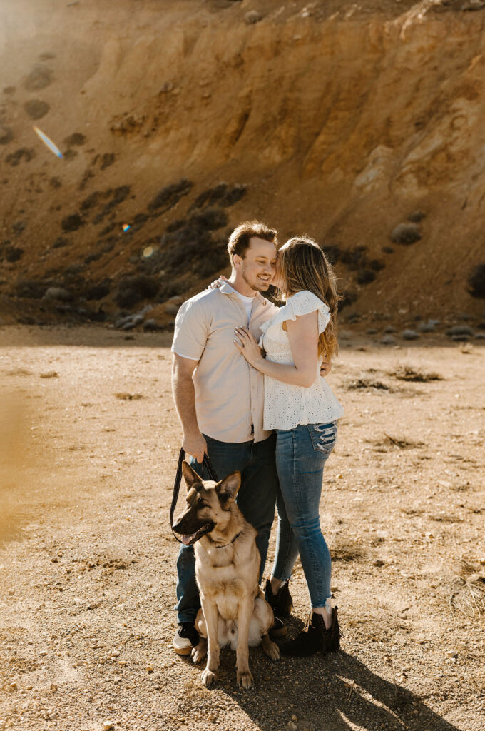 Engagement couple holding each other while dog sits in front of them outside virginia city