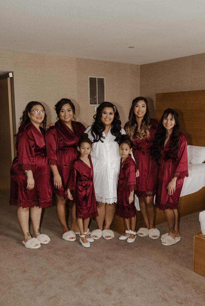 bride and bridesmaids smiling at the camera in maroon robes at the whitney peak hotel