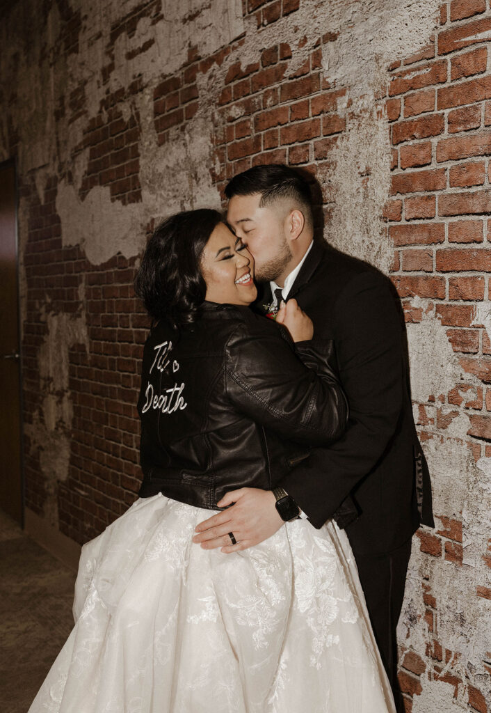 groom kissing the bride while she smiles wearing a til death leather jacket