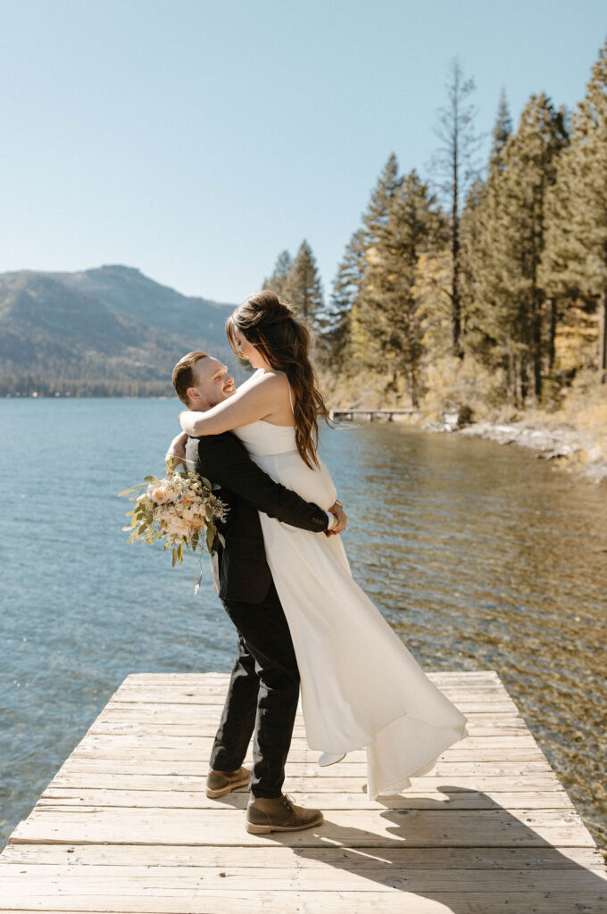 Elopement couple standing on dock on Donner lake while husband picks up wife smiling at each other