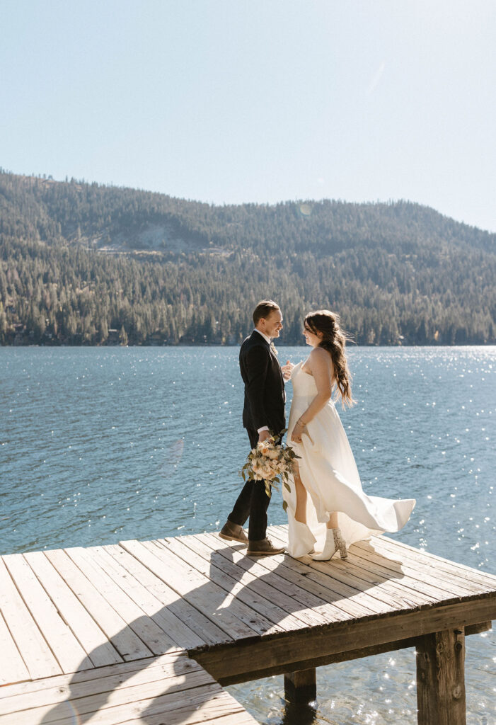 Elopement couple standing on dock together while holding hands and looking at each other with Donner lake and mountains in background