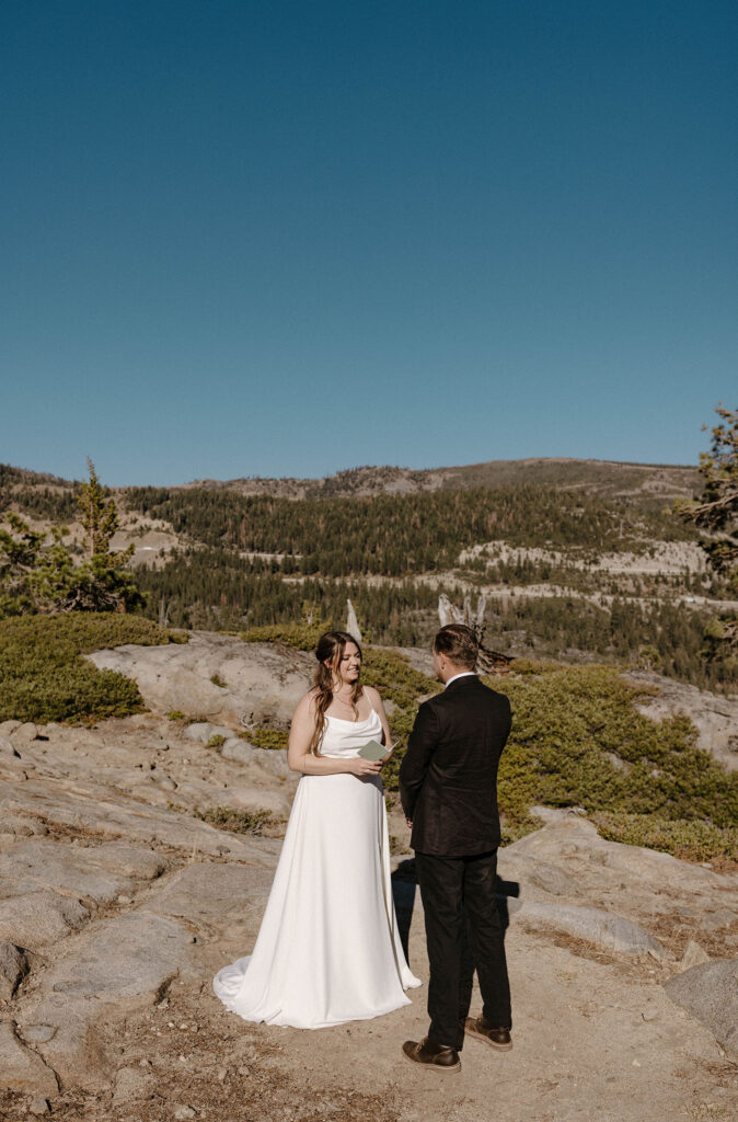 Elopement couple standing on rocks with mountains in background while reading vows to each other