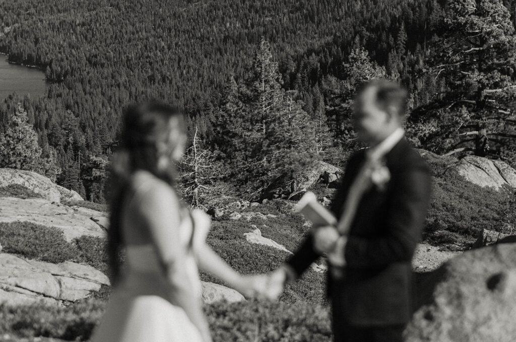 Elopement couple holding hands while reading vows to each other with trees and mountains in background