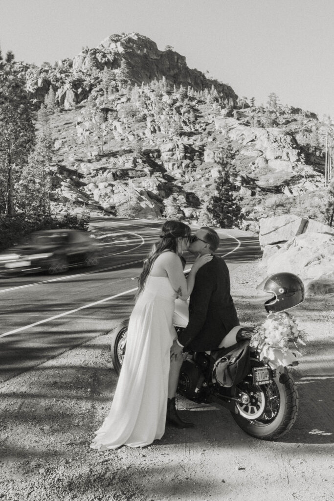 Elopement couple kissing while on motorcycle next to the road with helmet and flower bouquet