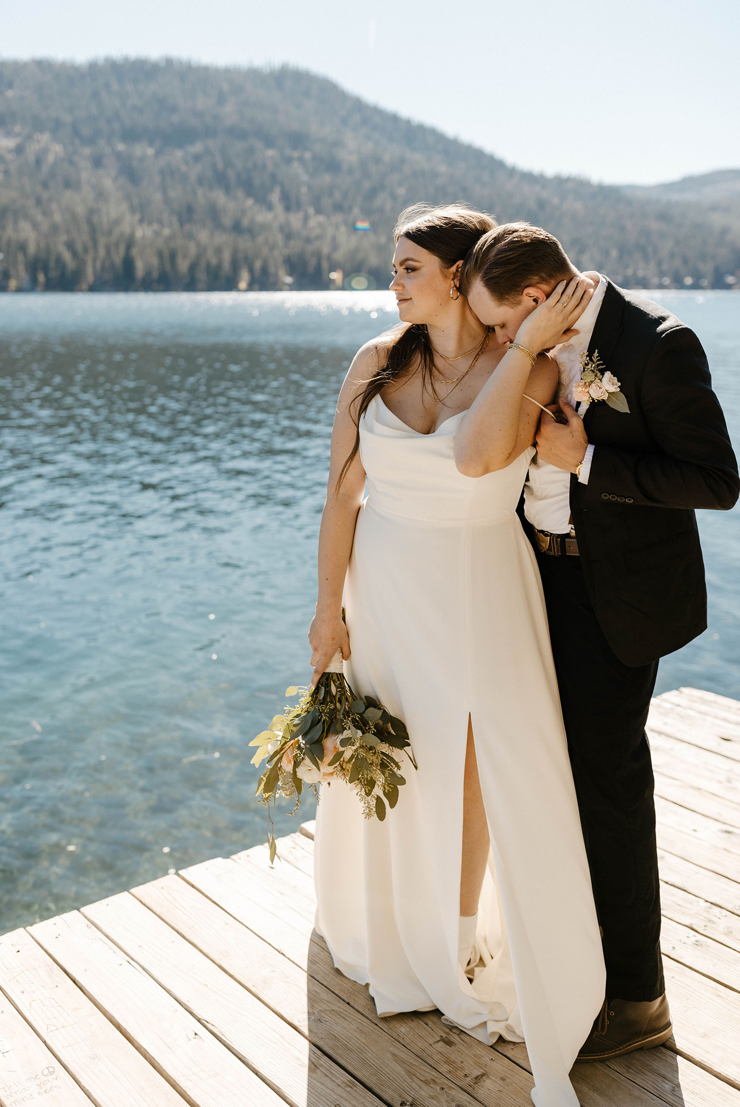 elopement couple standing on a dock overlooking donner lake while groom kisses her neck