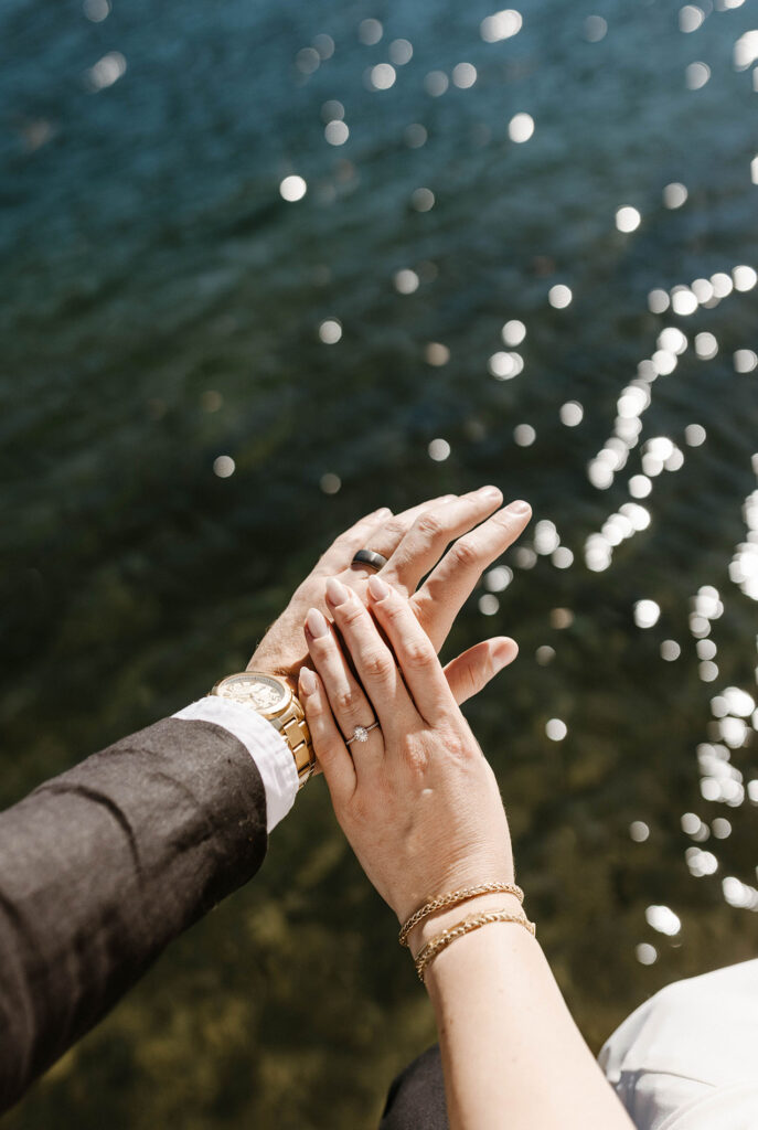 Close up of elopement couple's hands with wedding rings and water in background at Donner lake
