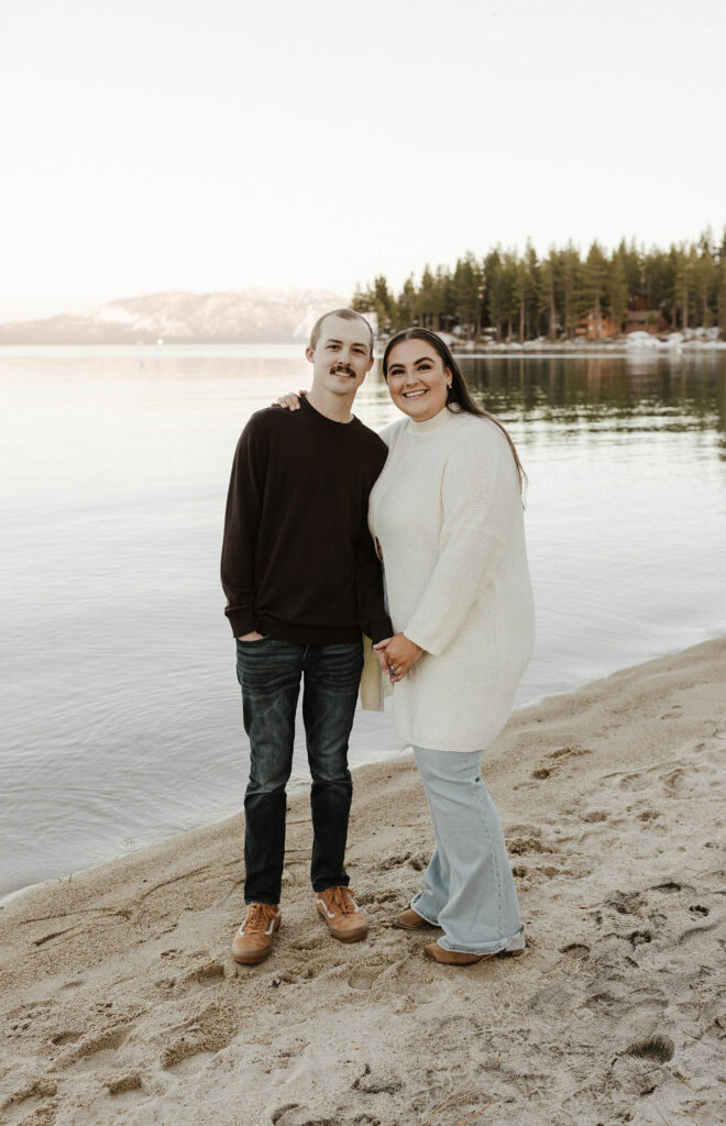 Engagement couple holding hands while looking at camera in meeks bay in Lake Tahoe
