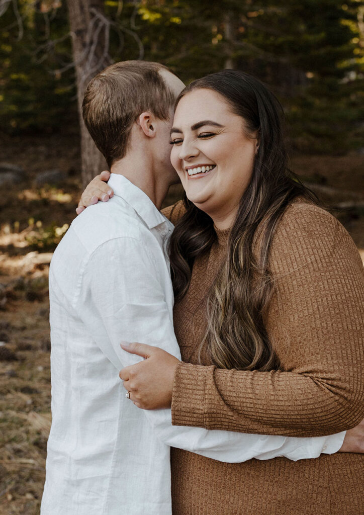 Woman laughing and smiling as fiancé hugs her in Lake Tahoe forest