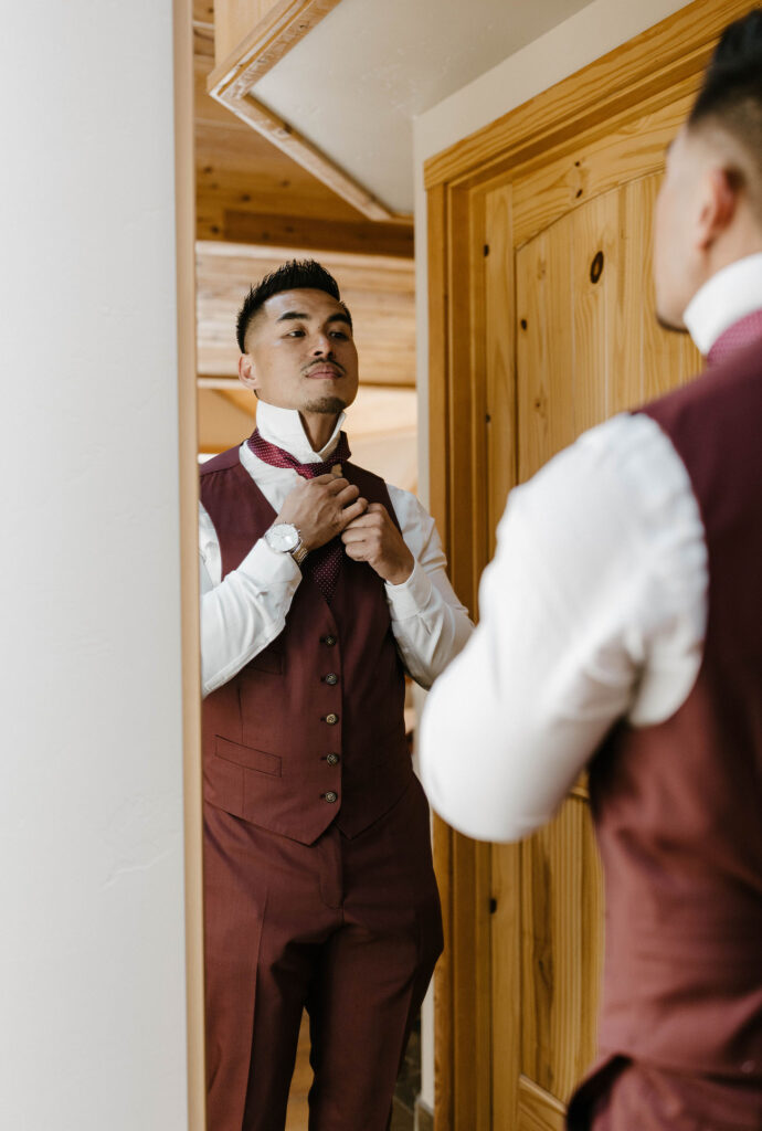Wedding groom tying tie while looking in mirror inside at the Chalet View Lodge