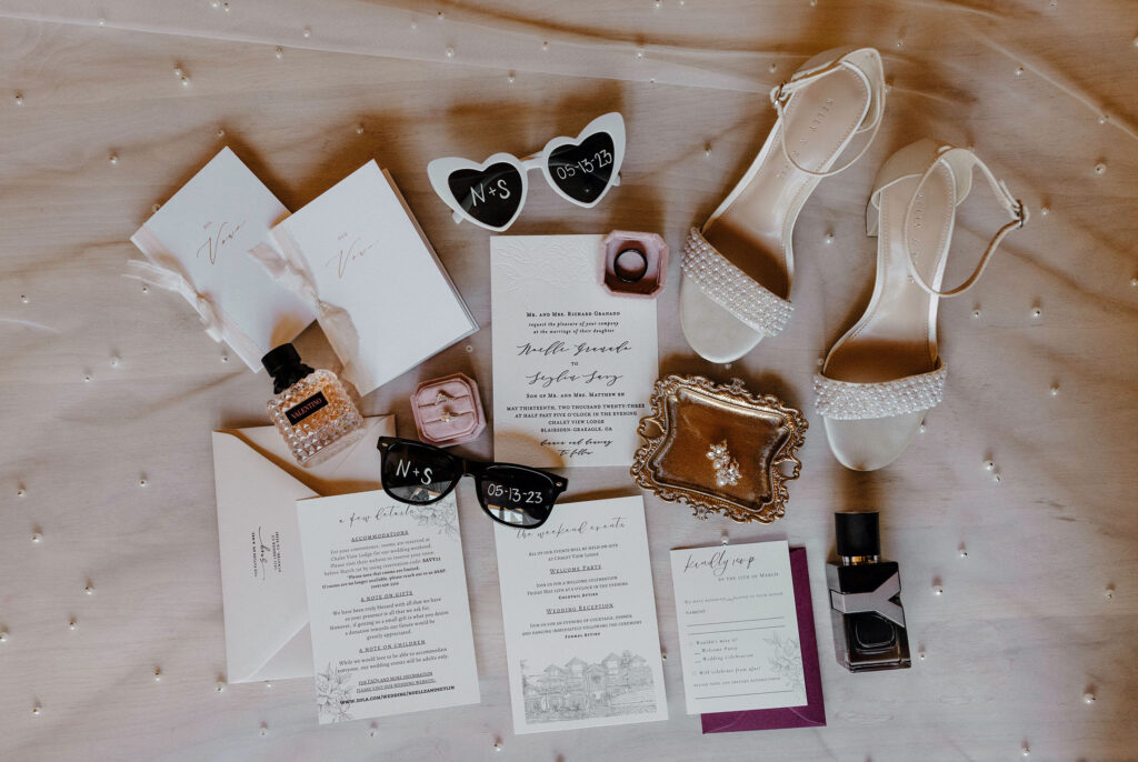 Wedding detail flat lay with shoes and invitations on white sheet at the Chalet View Lodge